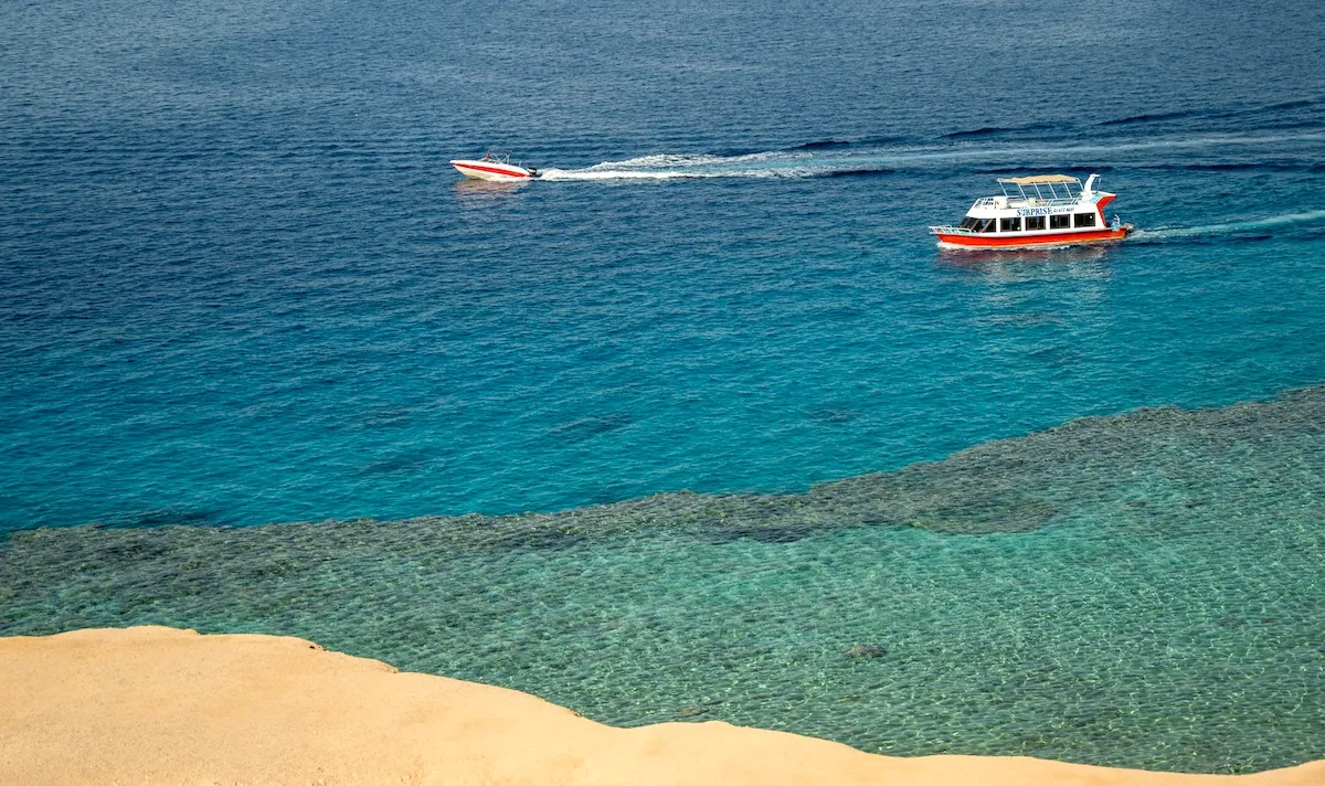 Two boats crossing the Red Sea off Sahl Hasheesh, above the edge of a reef seen through clear turquoise water