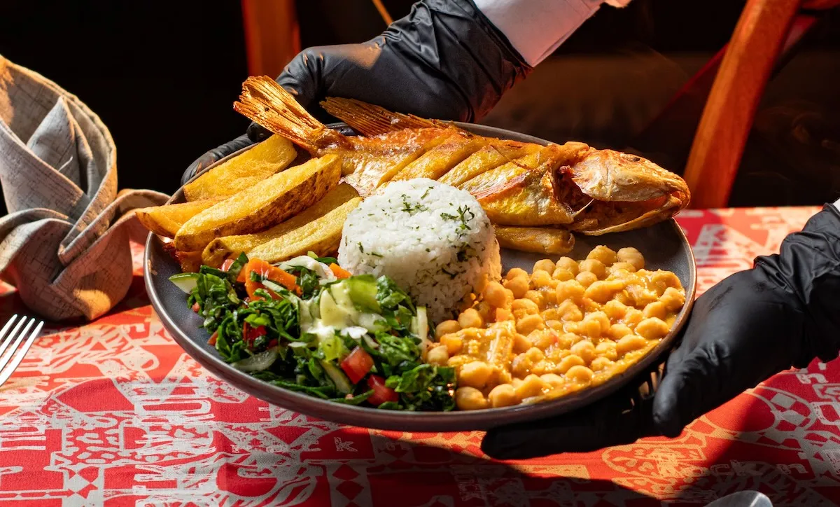 A waiter serving fried fish with rice, potato wedges, chickpeas and salad at a restaurant in Hurghada